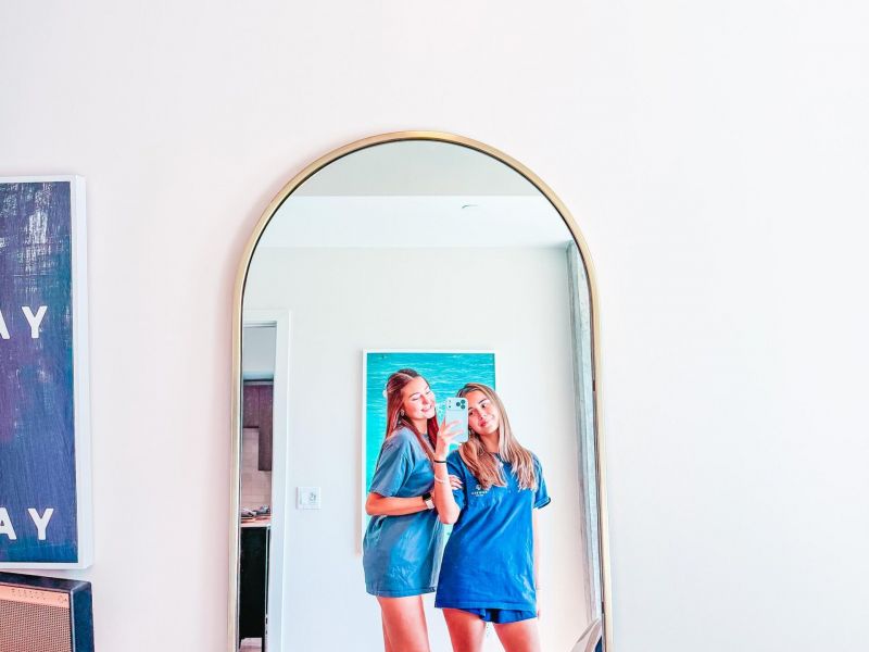 Rev Student Living Apartments Two women in blue outfits take a mirror selfie in a bright, modern bedroom with minimal decor and a cozy atmosphere.
