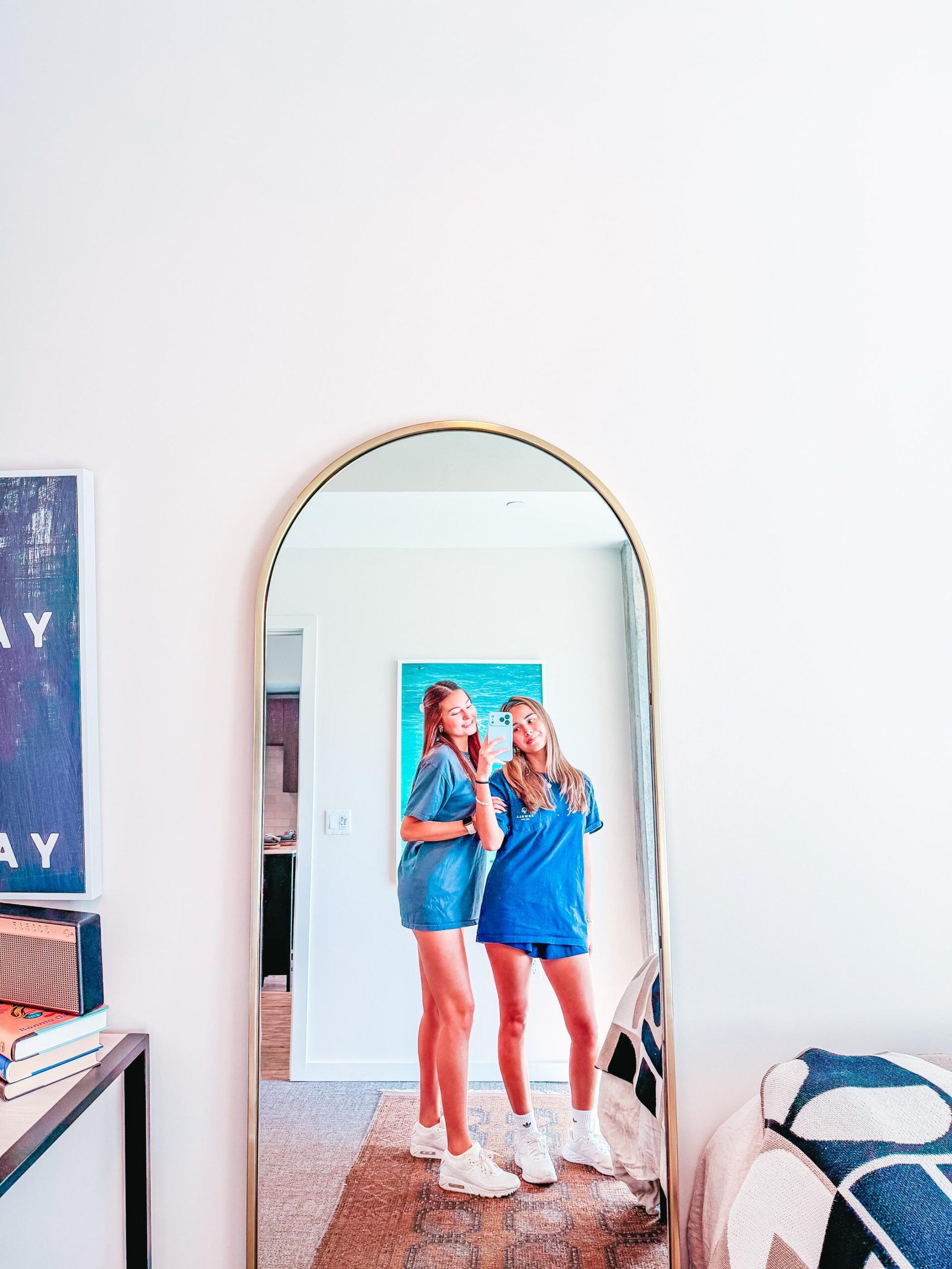 Rev Student Living Apartments Two women in blue outfits take a mirror selfie in a bright, modern bedroom with minimal decor and a cozy atmosphere.