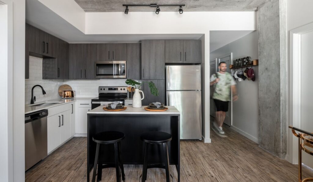 Rev Student Living Kitchen with Stainless Steel Appliances and Gray Cabinets with Student Walking